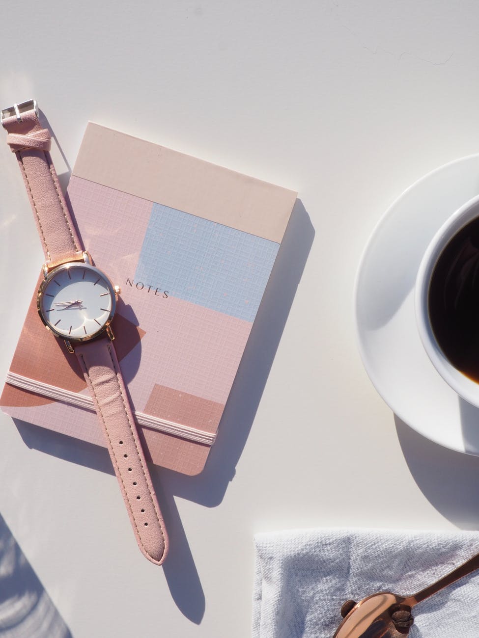 round gold colored analog watch with pink leather strap on pink notebook